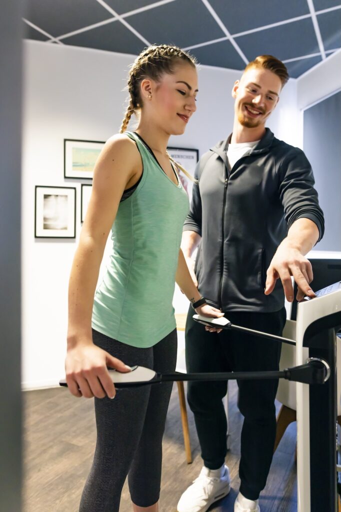 Young woman with personal trainer in fitness gym on body analysis device